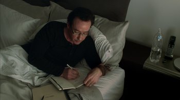 Movie still from “Maps to the Stars” (2014), directed by David Cronenberg – A man is writing in a notebook while laying in a bed; Close Up shot, Overhead angle