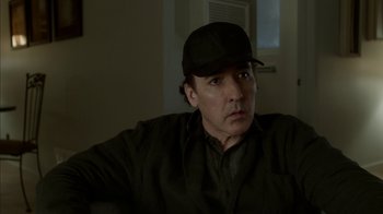 Movie still from “Maps to the Stars” (2014), directed by David Cronenberg – A man wearing a black hat sitting in front of a door; Close Up shot, Over the shoulder angle