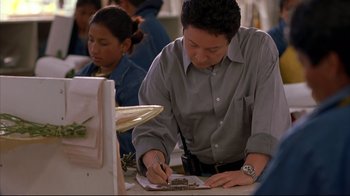 Movie still from “Maria Full of Grace” (2004), directed by Joshua Marston – A man writing on a piece of paper in front of a woman; Medium shot, High angle