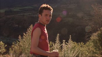 Movie still from “Maria Full of Grace” (2004), directed by Joshua Marston – A man in a red shirt is standing in the grass; Medium shot, Low angle