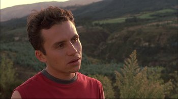Movie still from “Maria Full of Grace” (2004), directed by Joshua Marston – A man in a red t - shirt is standing in front of some trees; Close Up shot, Over the shoulder angle