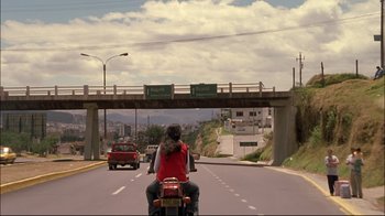 Movie still from “Maria Full of Grace” (2004), directed by Joshua Marston – A person riding a motorcycle down a street; Wide shot, Low angle