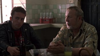 Movie still from “Maria Full of Grace” (2004), directed by Joshua Marston – A man sitting at a table with another man in front of him; Medium shot, Over the shoulder angle