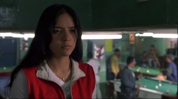 Movie still from “Maria Full of Grace” (2004), directed by Joshua Marston – A woman in a red jacket standing in front of a group of people; Close Up shot, Over the shoulder angle