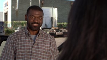 Movie still from “Maria Full of Grace” (2004), directed by Joshua Marston – A man in a plaid shirt smiling at the camera; Close Up shot, Over the shoulder angle
