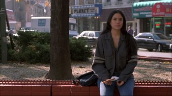 Movie still from “Maria Full of Grace” (2004), directed by Joshua Marston – A woman sitting on top of a bench near a tree; Medium shot, Over the shoulder angle