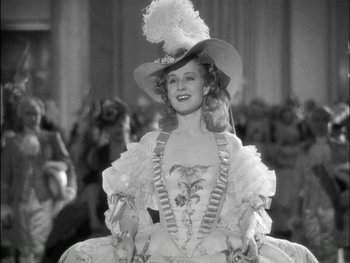Movie still from “Marie Antoinette” (1938), directed by Julien Duvivier – A woman wearing a fancy dress outfit and a hat; Medium shot, Low angle