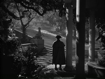 Movie still from “Marie Antoinette” (1938), directed by Julien Duvivier – A man in a black coat and a hat standing on steps; Extreme Wide shot, High angle