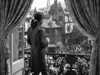 Movie still from “Marie Antoinette” (1938), directed by Julien Duvivier – A woman standing on a balcony looking out at a crowd of onlookers; Medium shot, Over the shoulder angle