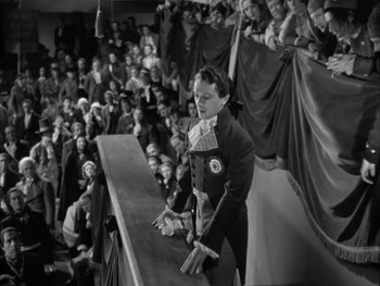 Movie still from “Marie Antoinette” (1938), directed by Julien Duvivier – A man standing in front of an audience in front of an audience; Wide shot, High angle