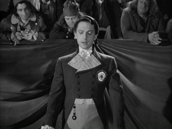 Movie still from “Marie Antoinette” (1938), directed by Julien Duvivier – A man in a suit and tie standing in front of a group of people; Medium shot, Low angle