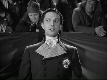 Movie still from “Marie Antoinette” (1938), directed by Julien Duvivier – A man in a suit and tie standing in front of a crowd; Medium shot, Low angle