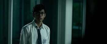 Movie still from “Extraction” (2020), directed by Sam Hargrave – A young man wearing glasses and a tie; Close Up shot, Low angle