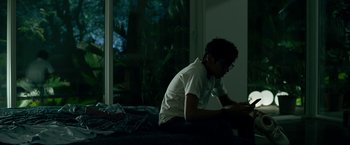 Movie still from “Extraction” (2020), directed by Sam Hargrave – A man sitting on a bed looking at his phone; Medium shot, Over the shoulder angle