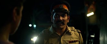 Movie still from “Extraction” (2020), directed by Sam Hargrave – A man in a police uniform is smiling for the camera; Close Up shot, Low angle