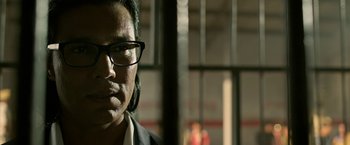 Movie still from “Extraction” (2020), directed by Sam Hargrave – A man wearing glasses and a suit; Close Up shot, Low angle