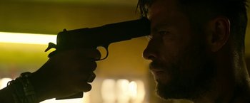 Movie still from “Extraction” (2020), directed by Sam Hargrave – A person holding a gun; Close Up shot, Over the shoulder angle