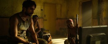 Movie still from “Extraction” (2020), directed by Sam Hargrave – A group of people sitting in a dimly - lit room; Medium shot, Over the shoulder angle