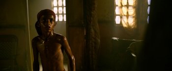Movie still from “Extraction” (2020), directed by Sam Hargrave – A shirtless man standing in a room next to a window; Medium shot, Low angle