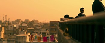 Movie still from “Extraction” (2020), directed by Sam Hargrave – A person sitting on a ledge looking out over a city; Wide shot, Low angle