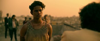 Movie still from “Extraction” (2020), directed by Sam Hargrave – A young man standing on top of a building; Close Up shot, Over the shoulder angle