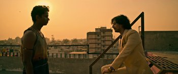 Movie still from “Extraction” (2020), directed by Sam Hargrave – A man sitting on a railing on top of a building; Medium shot, Low angle