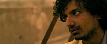 Movie still from “Extraction” (2020), directed by Sam Hargrave – A person with curly hair; Close Up shot, Over the shoulder angle