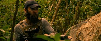 Movie still from “Extraction” (2020), directed by Sam Hargrave – A man with a beard is holding a rifle; Medium shot, Over the shoulder angle