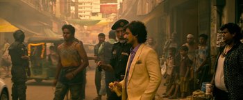 Movie still from “Extraction” (2020), directed by Sam Hargrave – A man in a yellow suit is standing next to another man; Medium shot, Over the shoulder angle