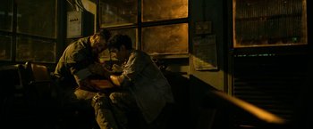 Movie still from “Extraction” (2020), directed by Sam Hargrave – A man sitting on top of a chair next to a woman; Medium shot, Over the shoulder angle