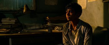 Movie still from “Extraction” (2020), directed by Sam Hargrave – A man sitting on a chair in a dark room; Medium shot, High angle