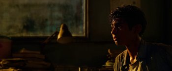 Movie still from “Extraction” (2020), directed by Sam Hargrave – A young man sitting in front of a window in the dark; Close Up shot, Low angle
