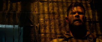 Movie still from “Extraction” (2020), directed by Sam Hargrave – A man with a beard is standing next to a brick wall; Close Up shot, Low angle