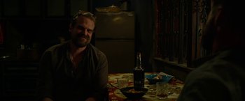 Movie still from “Extraction” (2020), directed by Sam Hargrave – A man sitting at a table with a bottle of wine; Medium shot, Over the shoulder angle