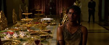 Movie still from “Extraction” (2020), directed by Sam Hargrave – A man sitting in front of a table with plates of food; Medium shot, High angle