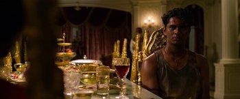 Movie still from “Extraction” (2020), directed by Sam Hargrave – A man sitting at a dinner table with wine glasses; Medium shot, Over the shoulder angle