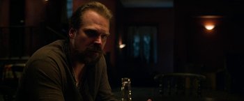 Movie still from “Extraction” (2020), directed by Sam Hargrave – A man sitting at a table with a drink in front of him; Close Up shot, Over the shoulder angle