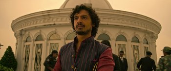 Movie still from “Extraction” (2020), directed by Sam Hargrave – A man with a beard is standing in front of a building; Close Up shot, Low angle