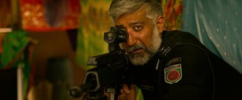 Movie still from “Extraction” (2020), directed by Sam Hargrave – A man with a beard is holding a rifle; Close Up shot, Low angle