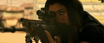 Movie still from “Extraction” (2020), directed by Sam Hargrave – A woman is holding a rifle and aiming it; Close Up shot, Over the shoulder angle