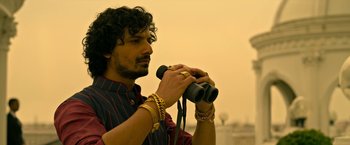Movie still from “Extraction” (2020), directed by Sam Hargrave – A man holding a pair of binoculars while wearing bracelets; Close Up shot, Low angle