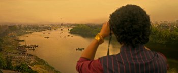 Movie still from “Extraction” (2020), directed by Sam Hargrave – A person looking out over a river at boats; Extreme Wide shot, High angle
