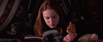 Movie still from “Mars Attacks!” (1996), directed by Tim Burton – A woman is reading a book while eating a piece of pizza; Close Up shot, High angle