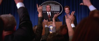 Movie still from “Mars Attacks!” (1996), directed by Tim Burton – A man is speaking at a podium in front of a crowd of onlookers; Medium shot, Low angle