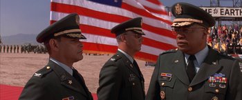 Movie still from “Mars Attacks!” (1996), directed by Tim Burton – A group of men standing in front of an american flag; Medium shot, Low angle