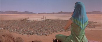 Movie still from “Mars Attacks!” (1996), directed by Tim Burton – A woman sitting on top of a rock in front of a crowd of people; Extreme Wide shot, High angle