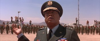 Movie still from “Mars Attacks!” (1996), directed by Tim Burton – A man in a military uniform is standing in front of a group of people; Close Up shot, Low angle