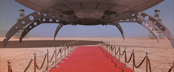 Movie still from “Mars Attacks!” (1996), directed by Tim Burton – A red carpet leading up to an airplane; Extreme Wide shot, High angle