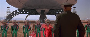 Movie still from “Mars Attacks!” (1996), directed by Tim Burton – A group of people dressed in green and red costumes; Medium shot, Over the shoulder angle
