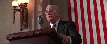 Movie still from “Mars Attacks!” (1996), directed by Tim Burton – An older man in a suit and tie speaking at a podium; Close Up shot, Low angle